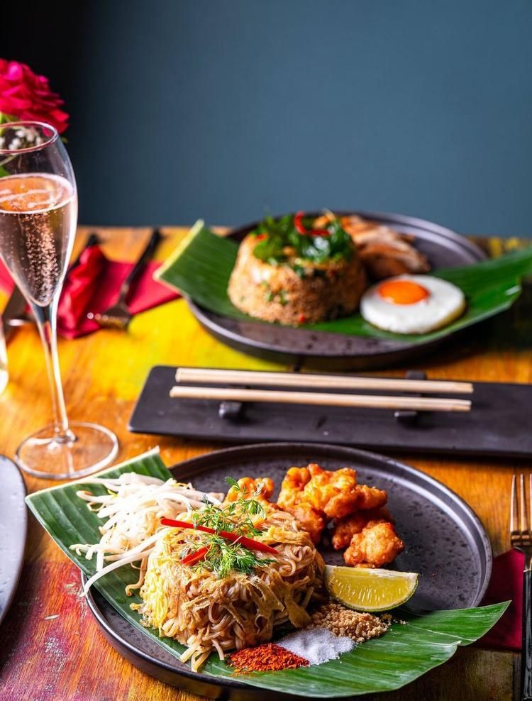 Thai curry and rice on banana leaves with chopsticks, on a restaurant table beside a glass of sparkling drink