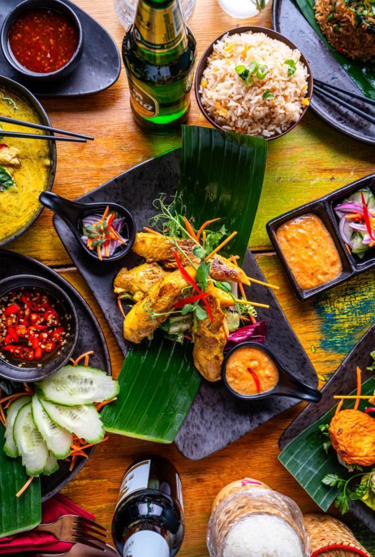 Colorful Indonesian meal spread on banana leaves with rice, grilled chicken, sauces, and sides on a wooden table