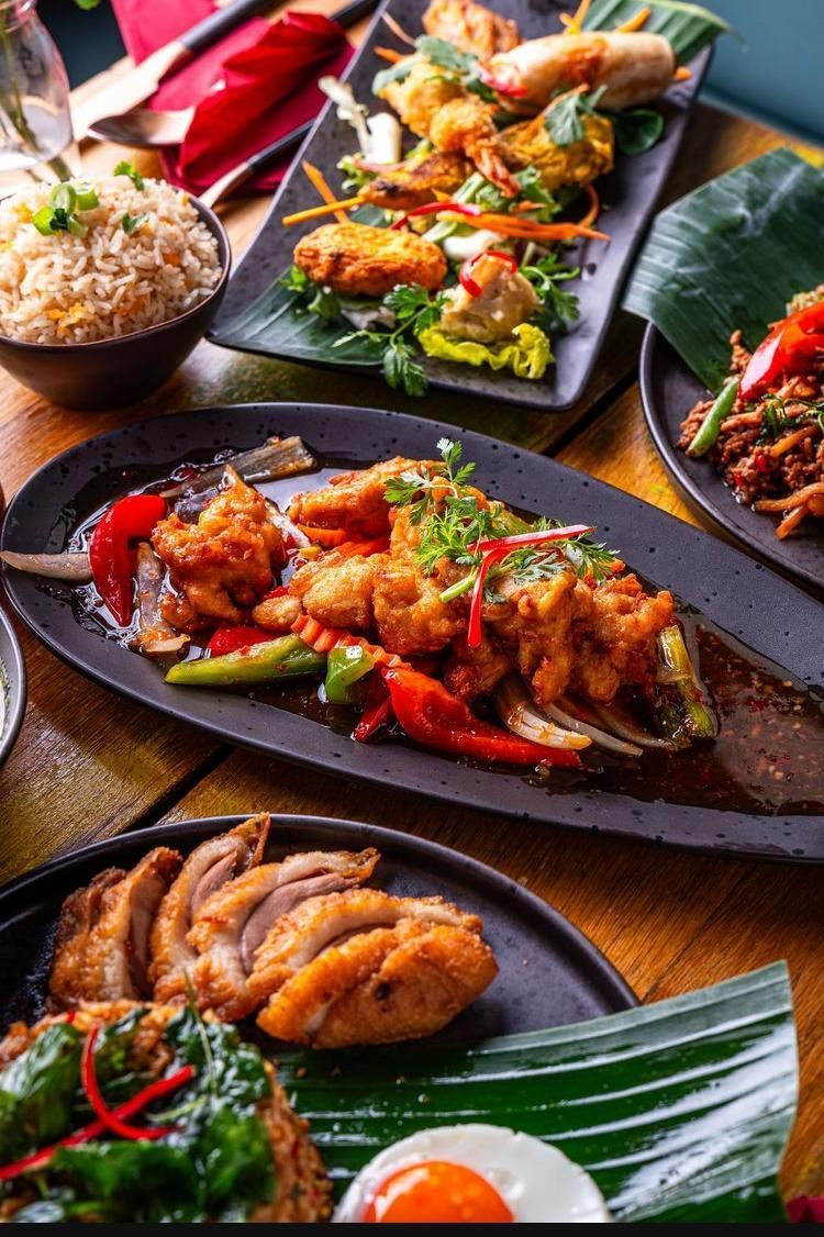 Assorted colorful plated dishes, including grilled chicken and vegetables, served on dark tableware.