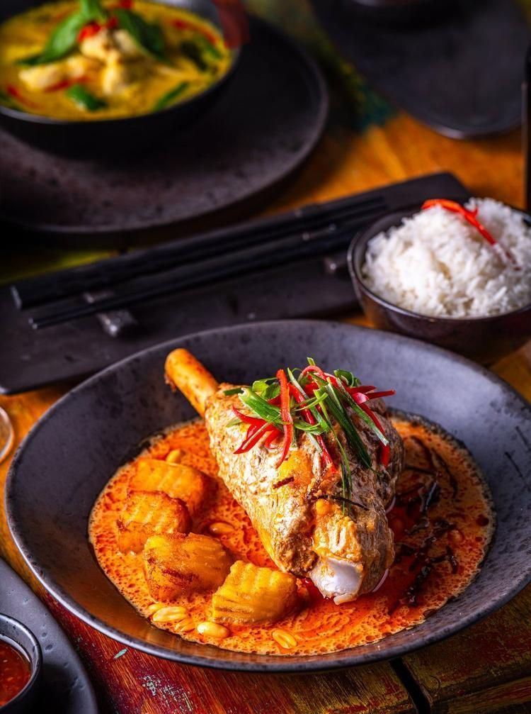 Plated fried fish with rice and vegetables on a dark table, with bowls in the background