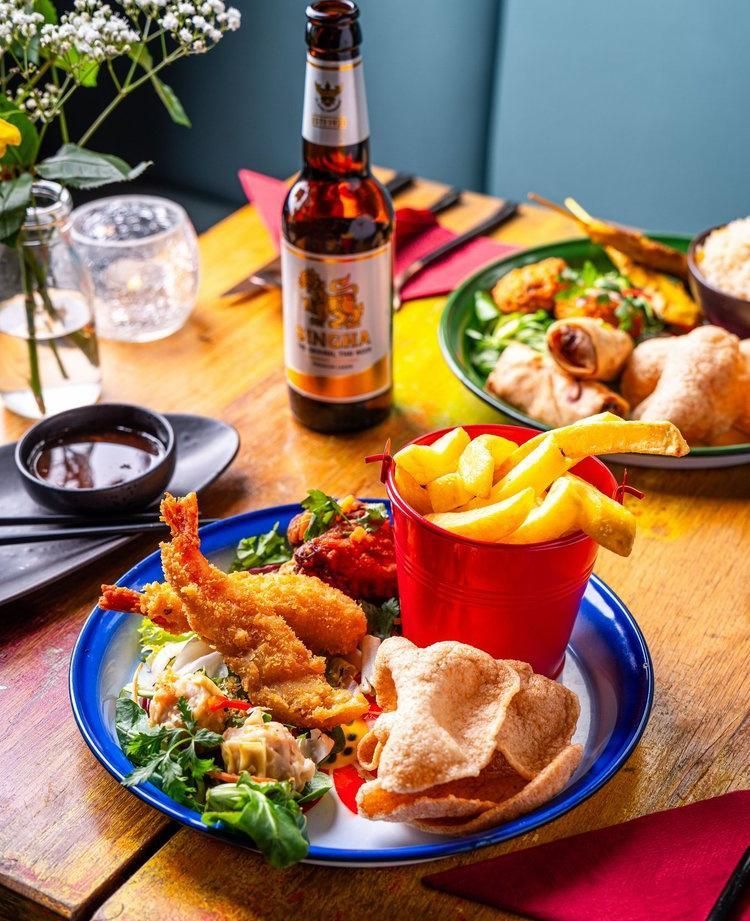 A table with fried food, fries, salad, drinks, and a bottle in a colorful restaurant setting
