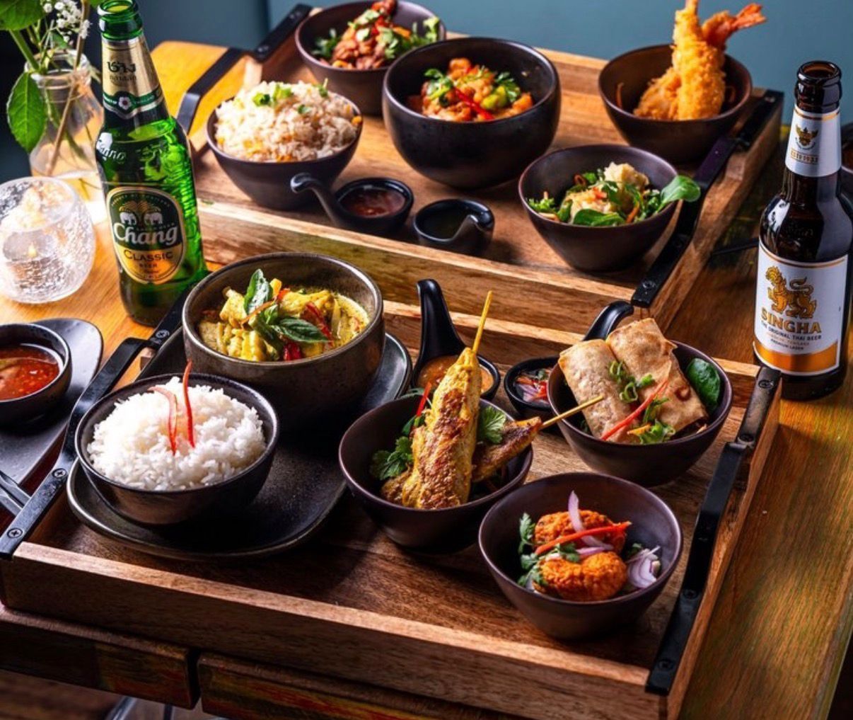 Japanese meal spread on wooden trays with rice, tempura, curry, and beer bottles