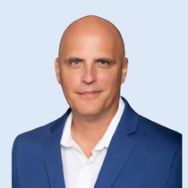 Man in blue blazer and white shirt, smiling, headshot.