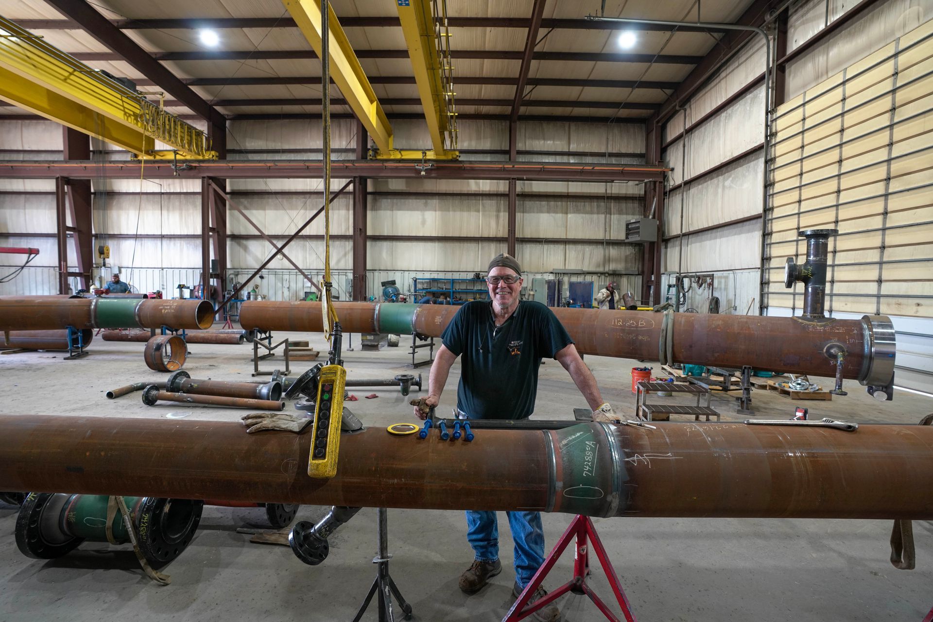 A man is standing next to a large pipe in a factory.