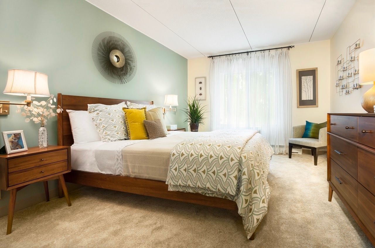 Bedroom in a modern apartment with a wooden bed frame, nightstands, dresser, and soft lighting.