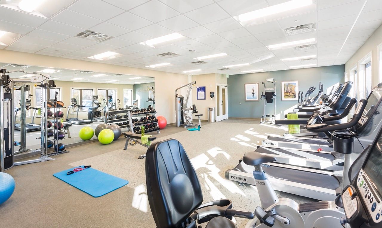 Bright on-site fitness center with treadmills, ellipticals, weights, and exercise balls.