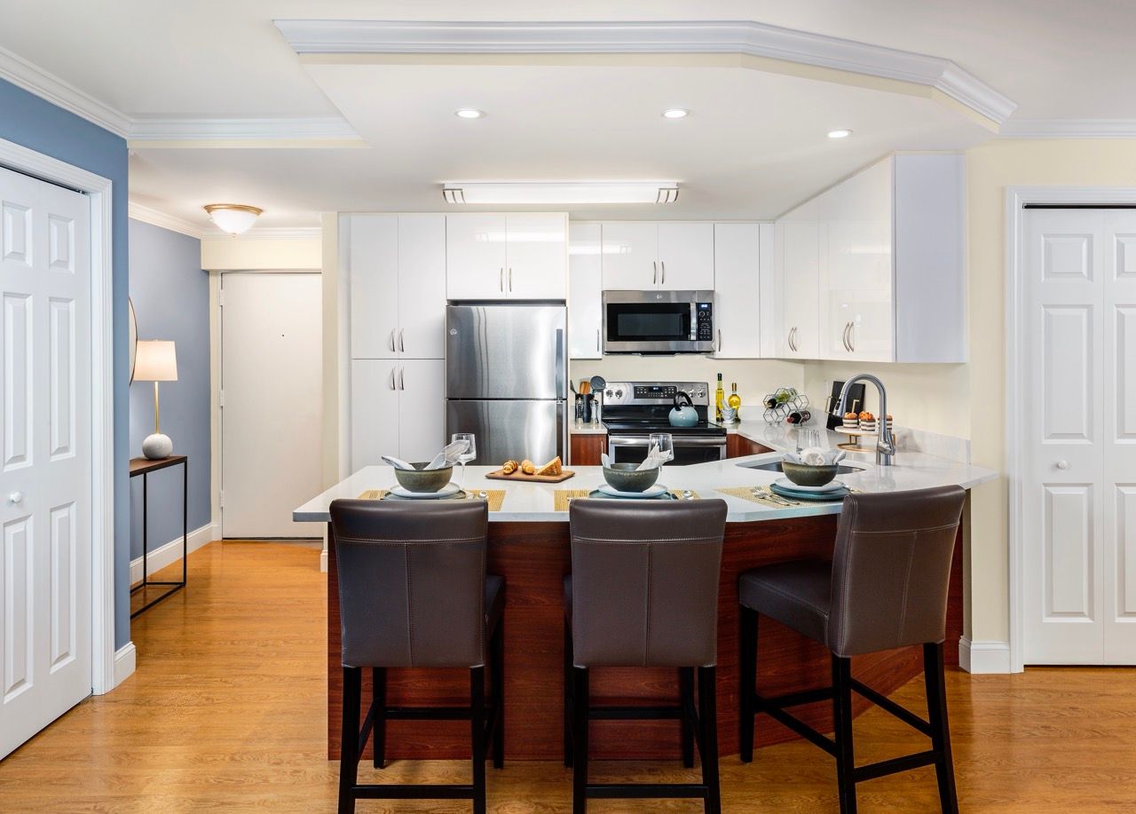 Modern kitchen with white cabinets, stainless steel appliances, and a wood island with four brown stools.