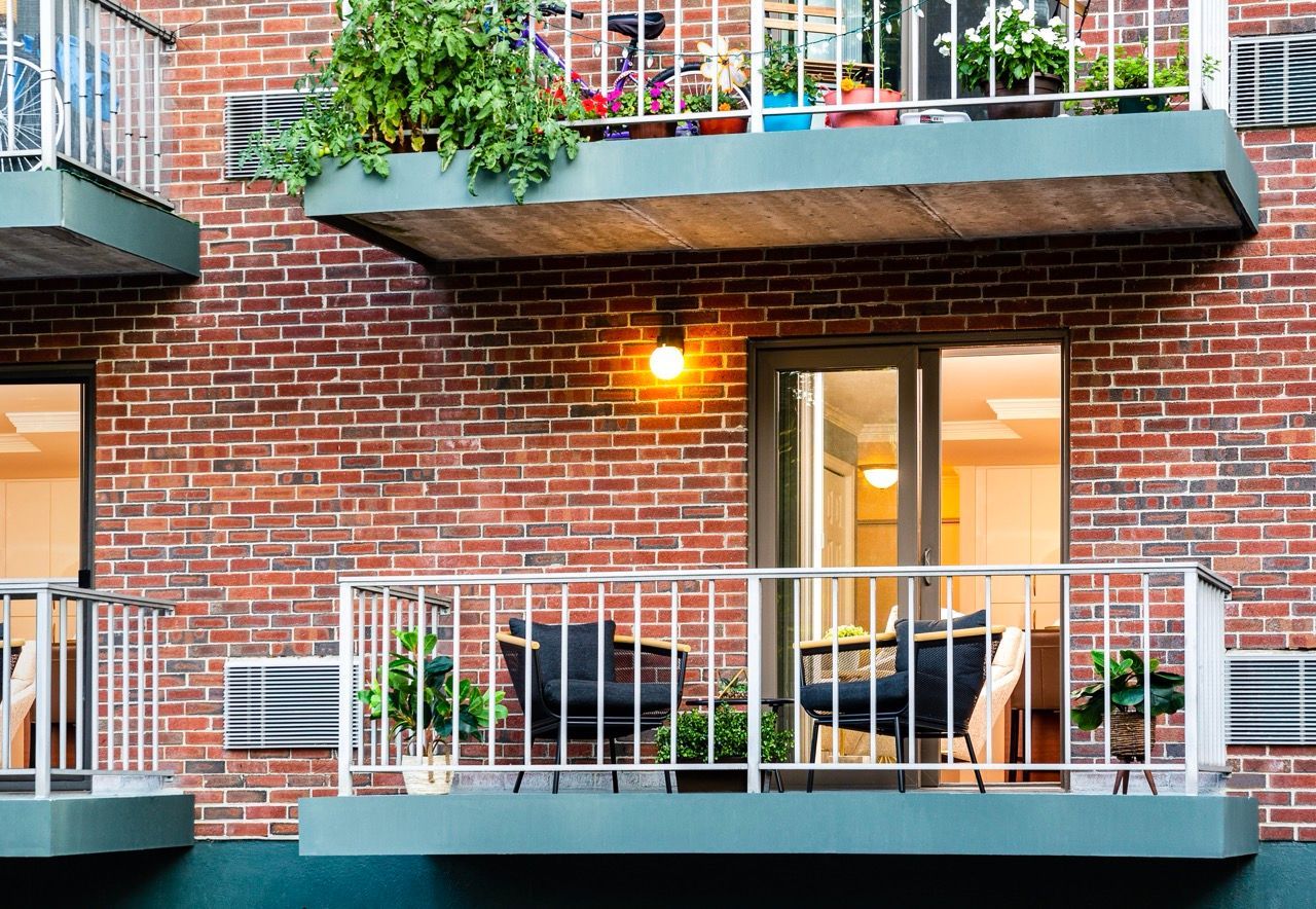 Brick apartment building exterior with a balcony, seating, and plants.