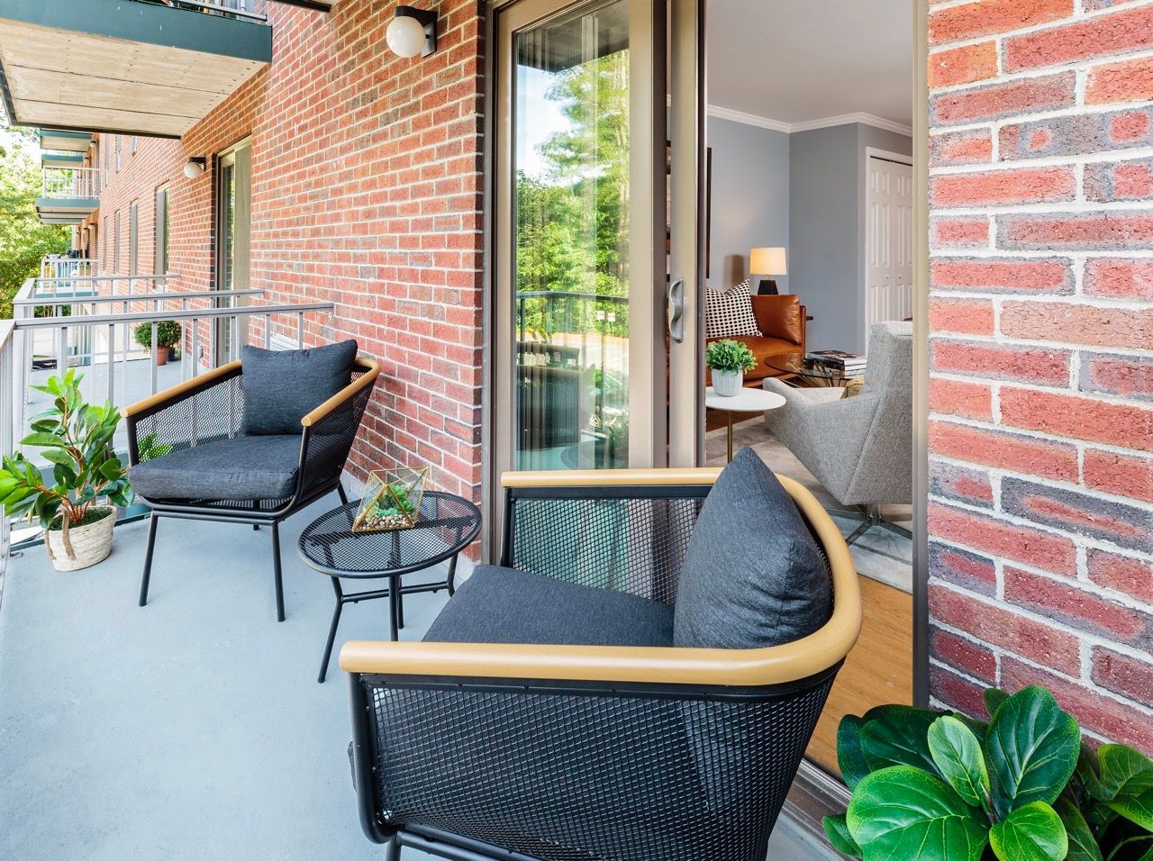 Balcony with black mesh furniture and a small table on a brick apartment building exterior.