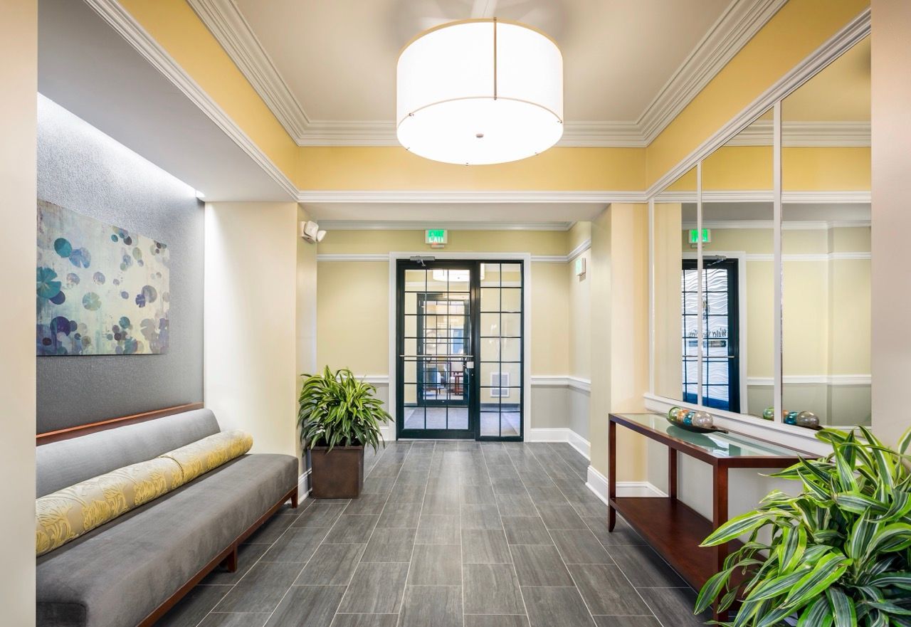 Interior apartment community lobby with bench seating, artwork, and potted plants.