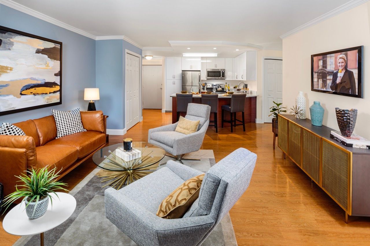 Open-concept living area with blue accent wall, brown leather sofa, and kitchen in the background.