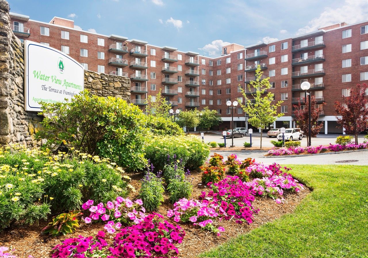Exterior view of Water View Apartments with brick building, sign, and lush landscaping.