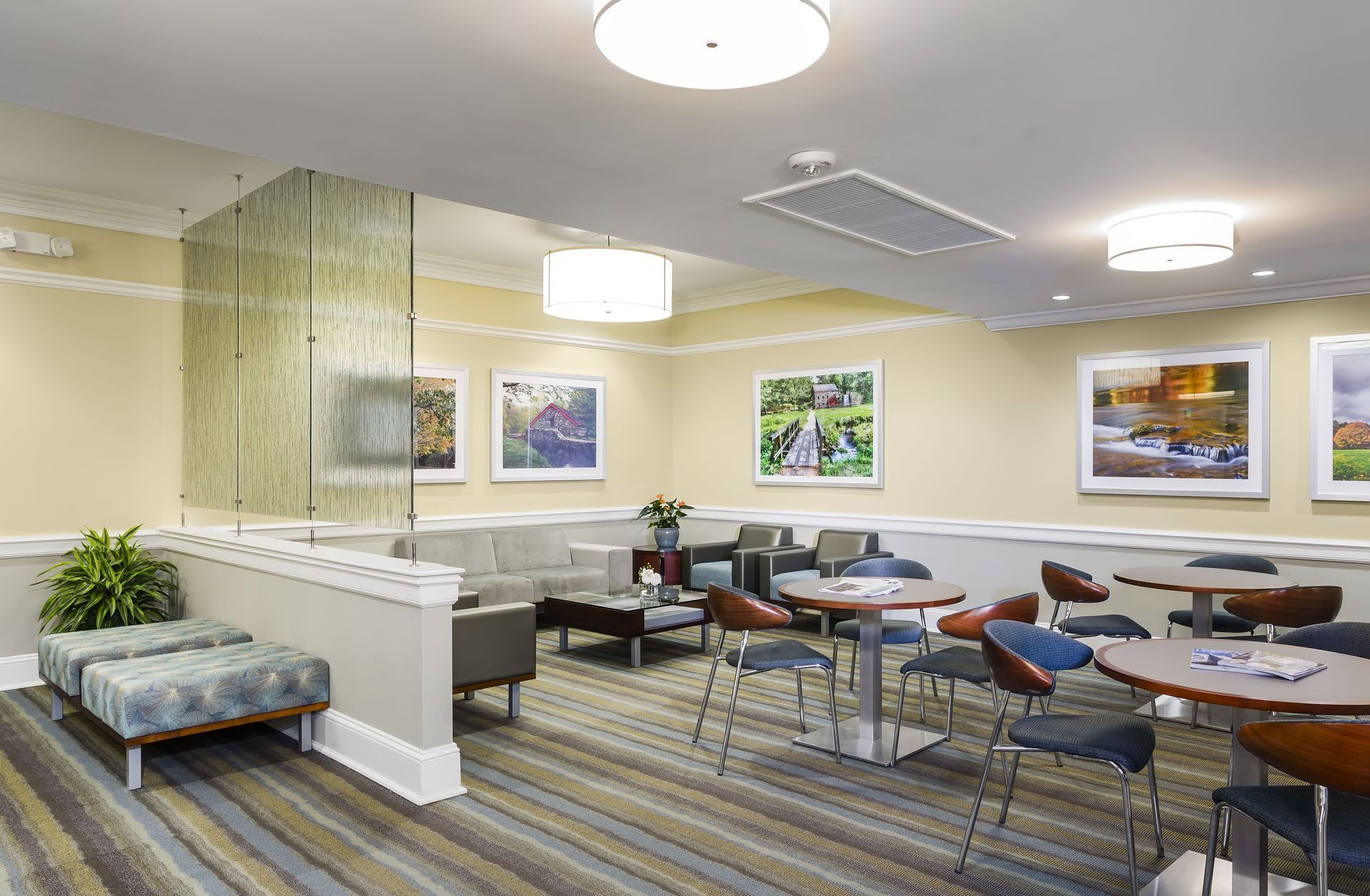 A seating area with tables, chairs, upholstered benches, and wall art, featuring neutral tones and warm lighting.