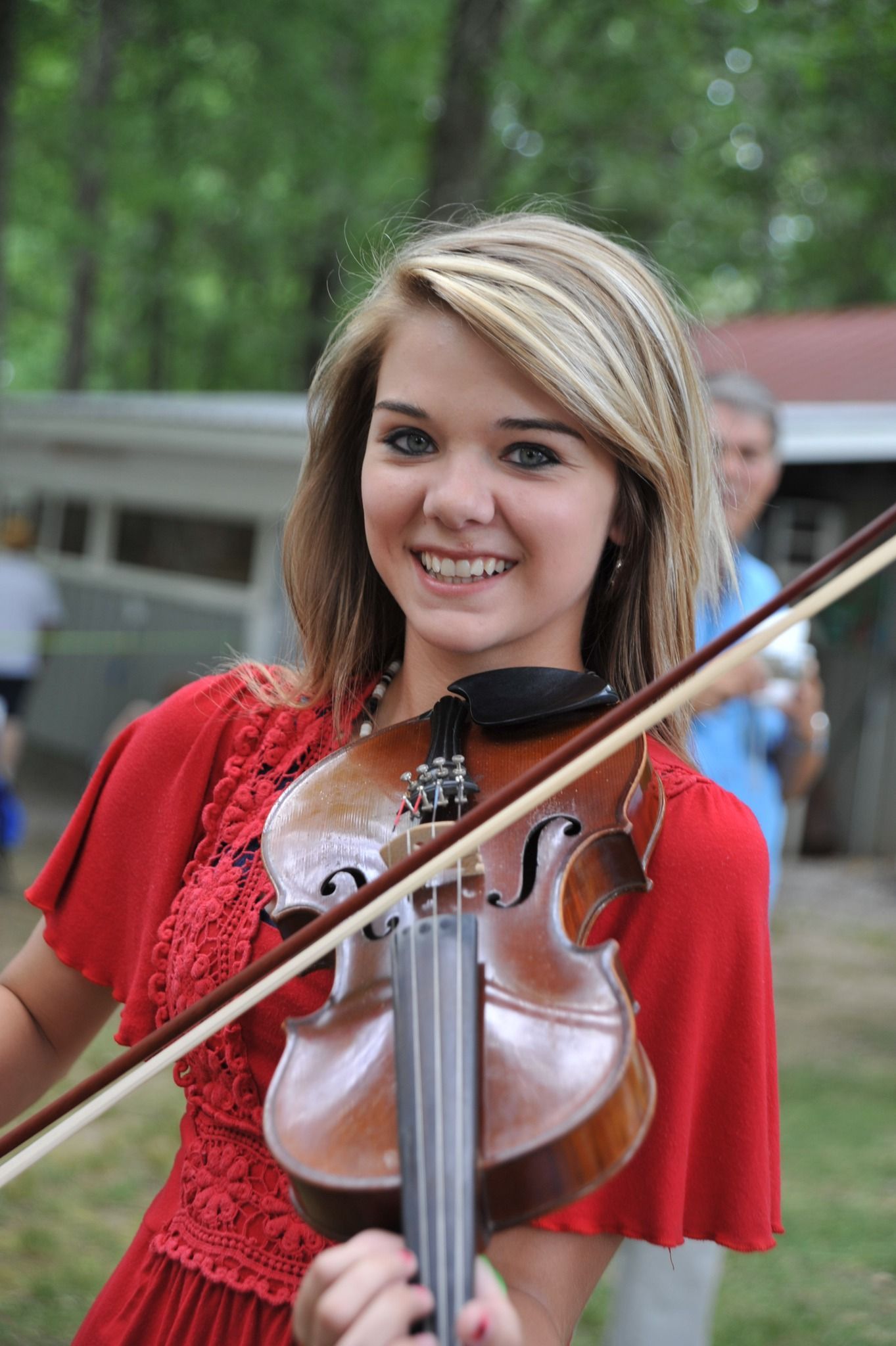 A young woman in a red dress is playing a violin.