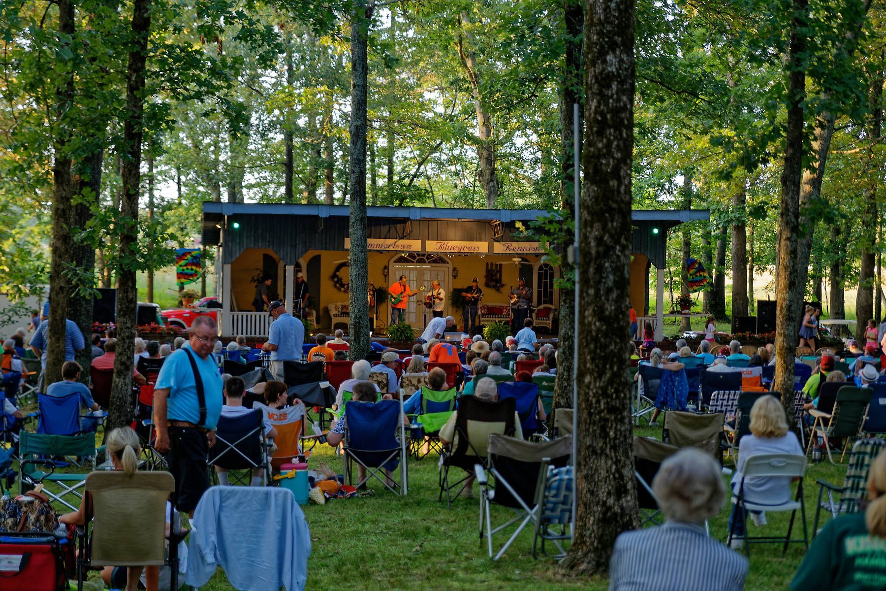 A group of people are sitting in chairs in front of a stage in the woods.