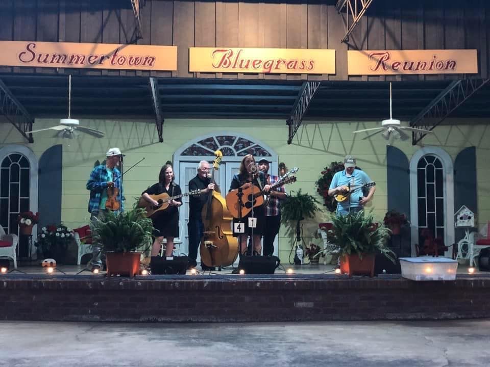 A group of people playing instruments on a stage under a sign that says summertown bluegrass reunion