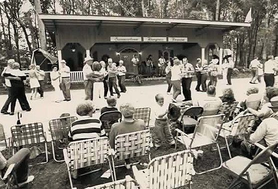 A black and white photo of a group of people dancing in front of a building.