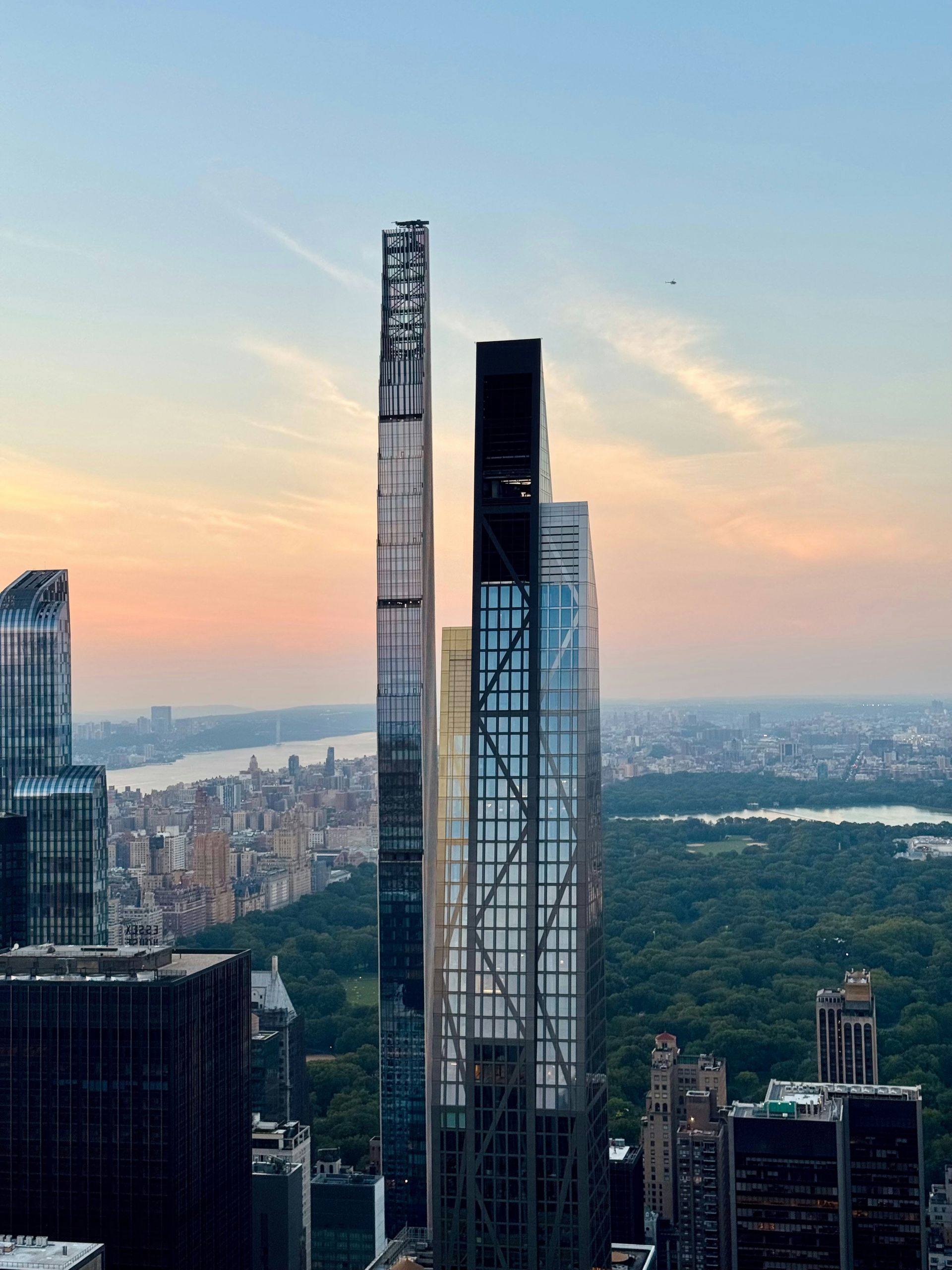 A high-angle view of slender skyscrapers in New York City at sunset, with Central Park visible in the background.