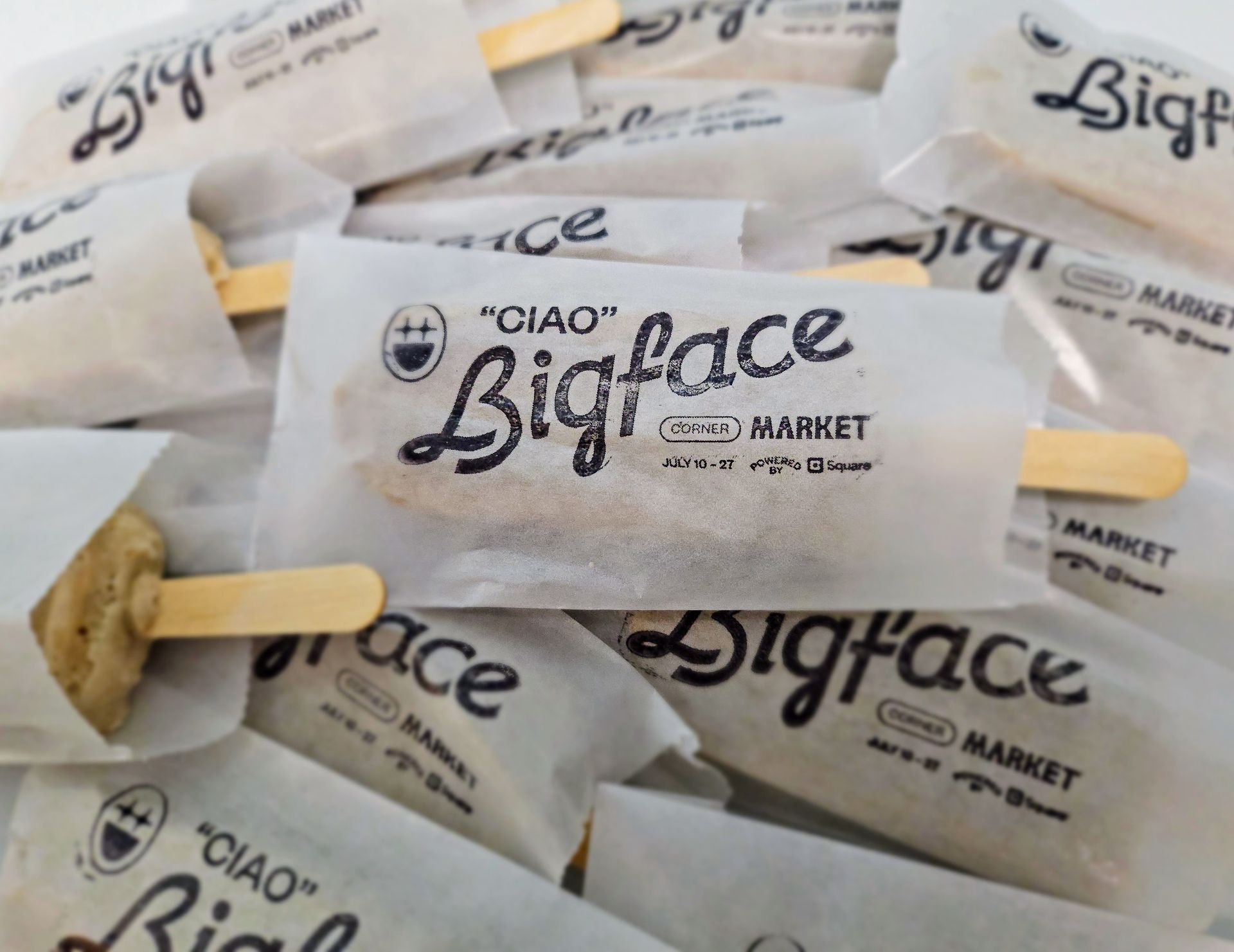Close-up of numerous wrapped frozen treats with wooden sticks. Each is labeled 