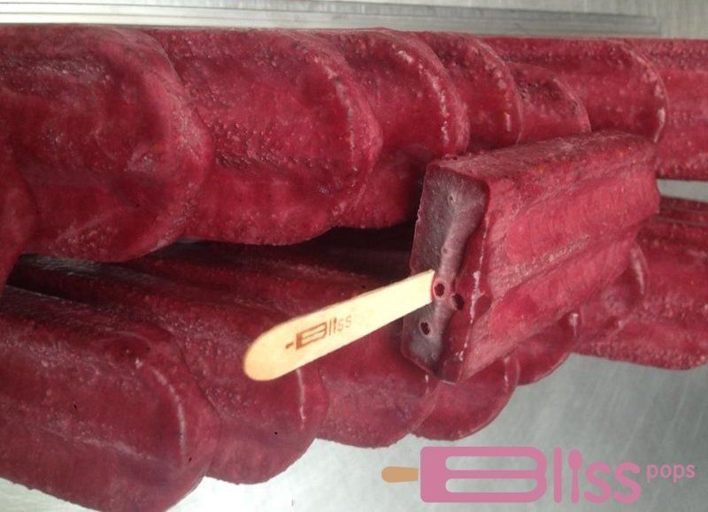 A close up of a red popsicle with a wooden stick