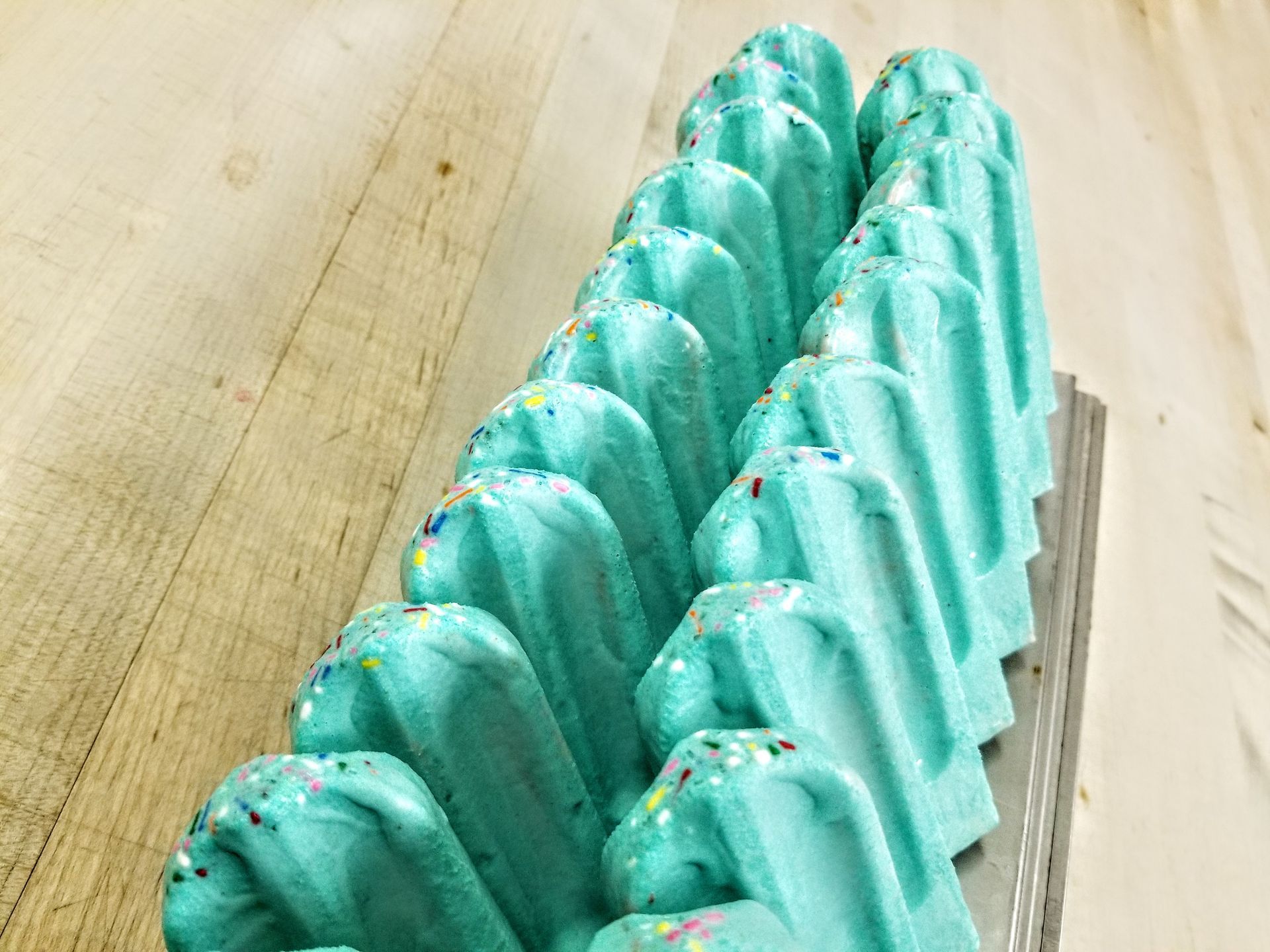 A row of blue popsicles with sprinkles on a wooden table.