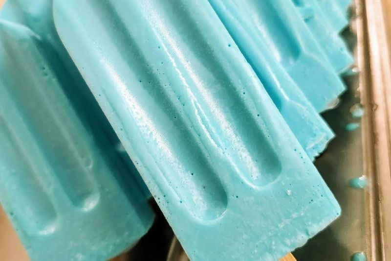 A row of blue popsicles are sitting on a table.