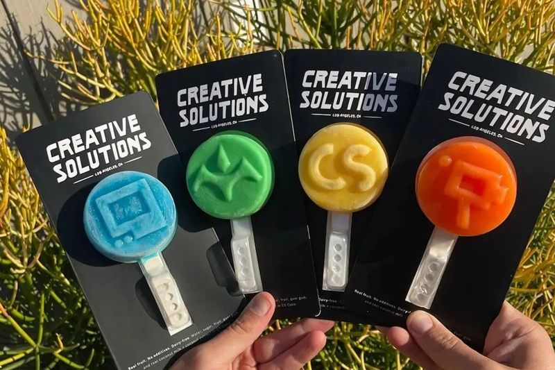 A person is holding three creative solutions lollipops in their hands