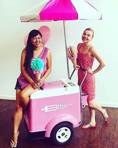 Two women are standing next to a pink ice cream cart.