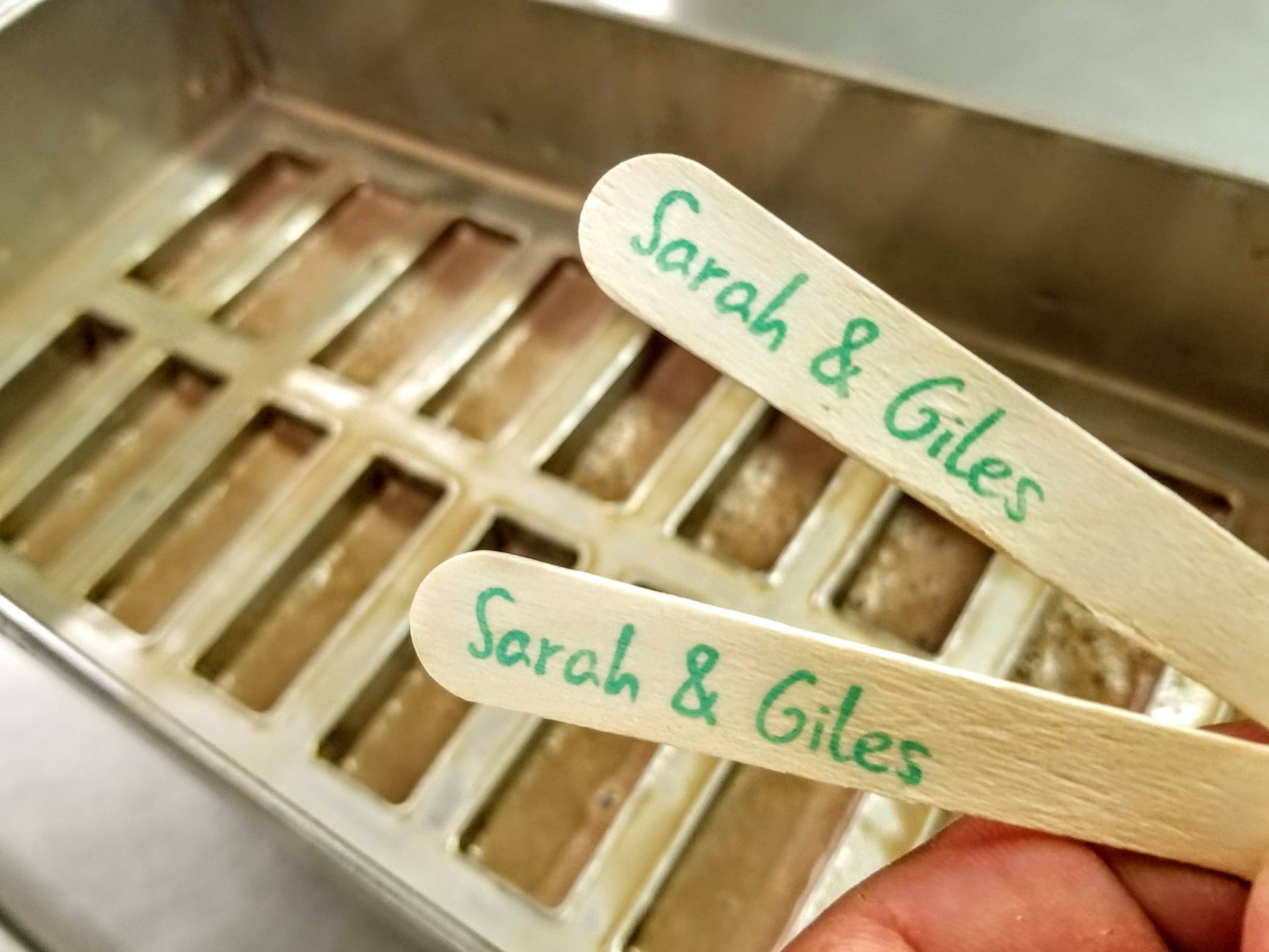 A person is holding two popsicle sticks that say sarah and giles