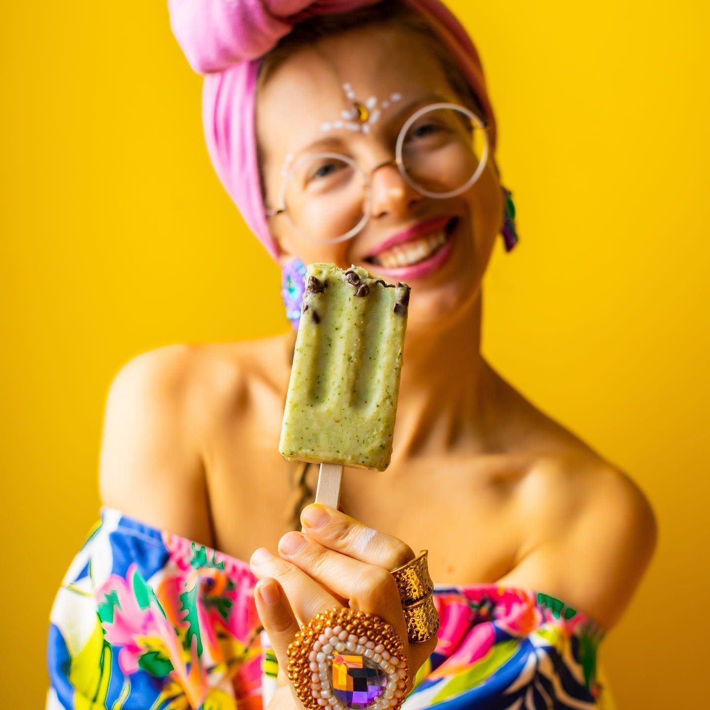 A woman wearing glasses and a pink headband is holding an ice cream bar.