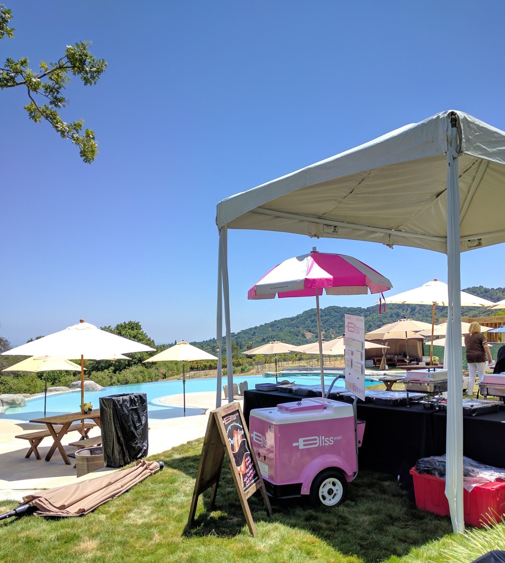 A pink and white ice cream cart is under a tent