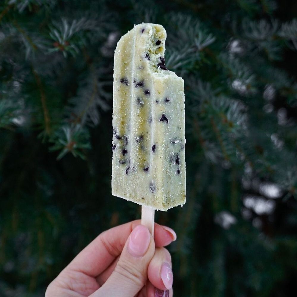 A person is holding a popsicle with a bite taken out of it.