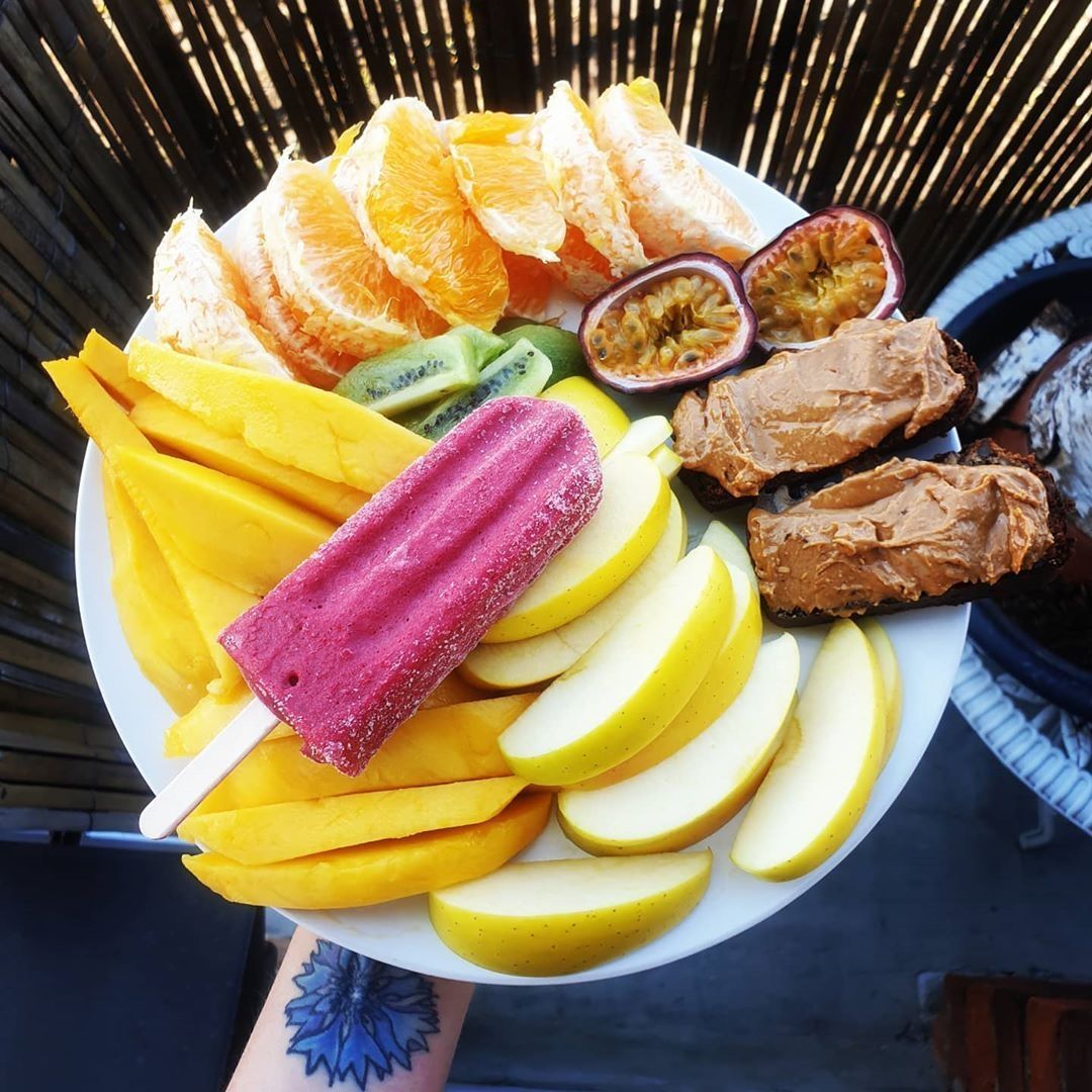 A person with a tattoo on their arm is holding a plate of fruit
