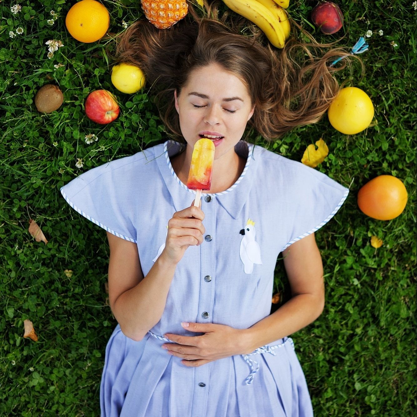 A woman is laying in the grass eating a popsicle