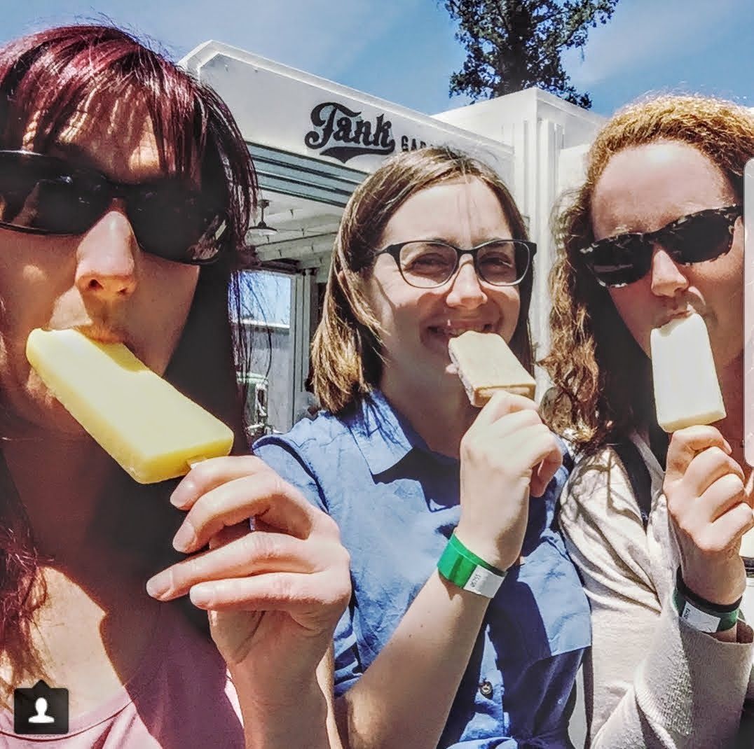 Three women are eating popsicles in front of a tank truck