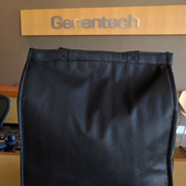 Black mesh drawstring pouch with a tan Genentech label above it on a wooden surface.