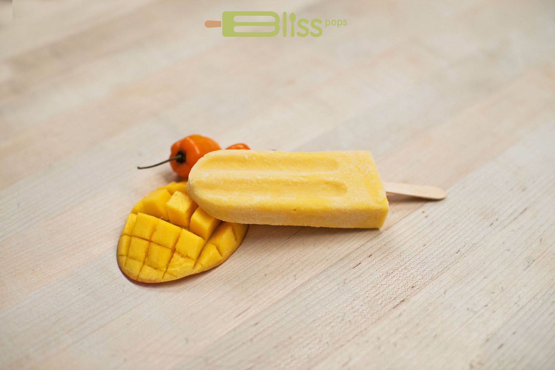 A mango popsicle is sitting on a wooden table next to a slice of mango.