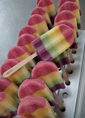 A row of rainbow colored popsicles with a wooden stick in the middle.