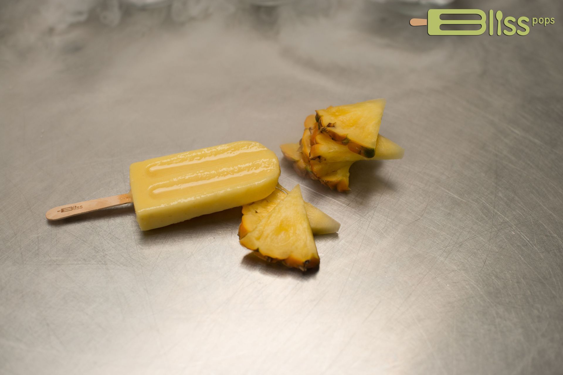 A pineapple popsicle is sitting on a metal surface next to a pineapple slice.