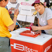 People sampling red pops from a Bliss Pops cart at an outdoor market.