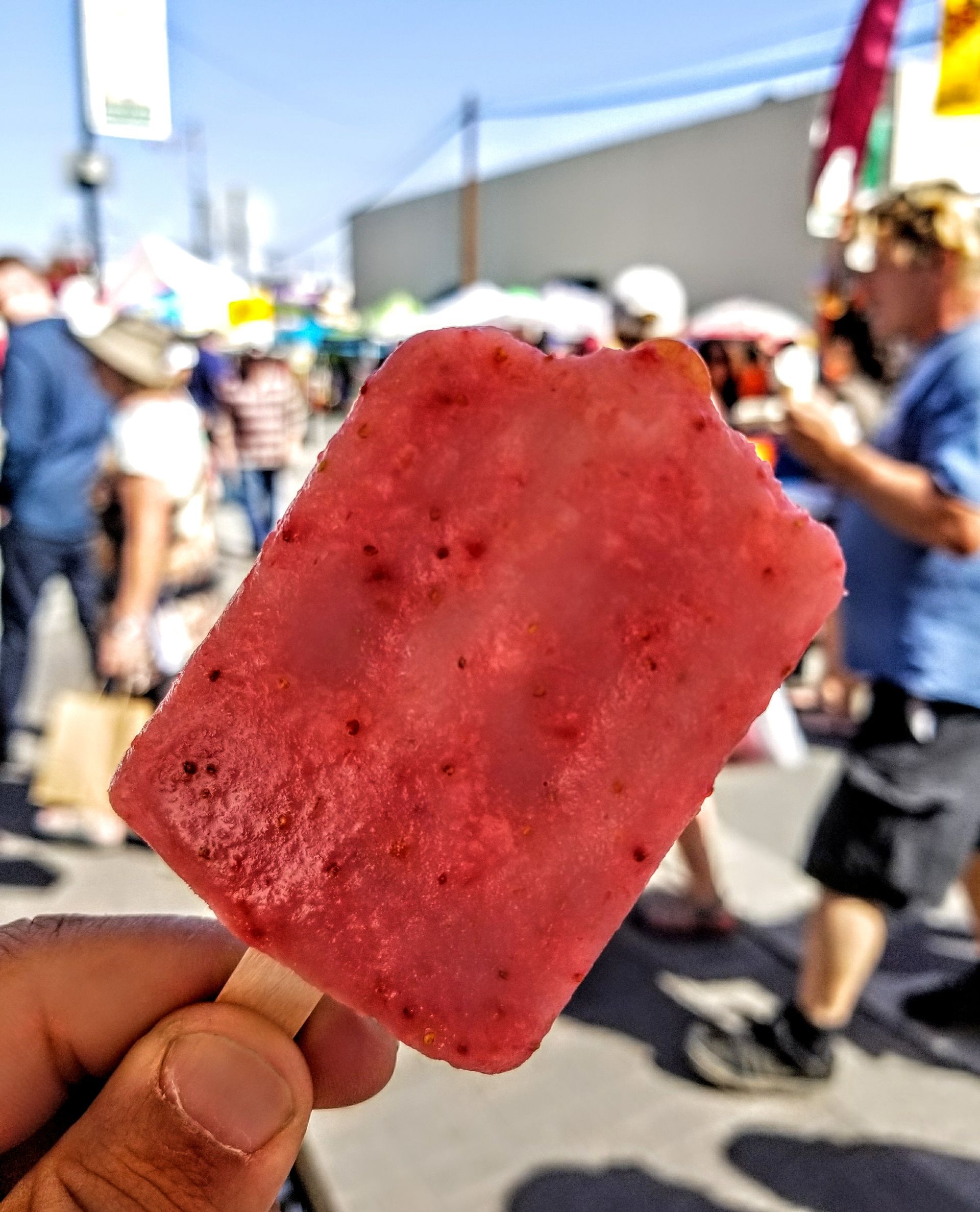 A person is holding a strawberry popsicle in their hand