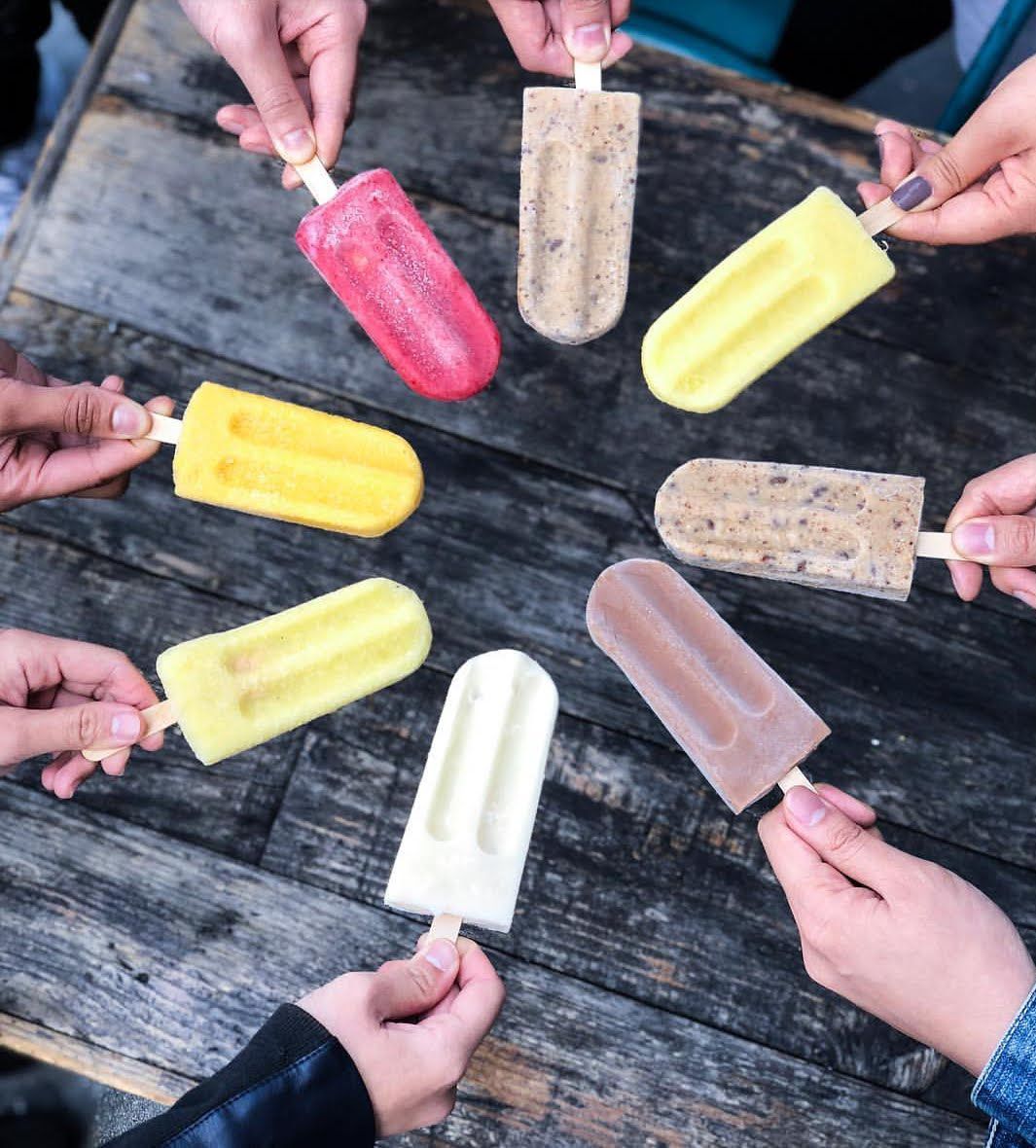 A group of people are holding popsicles in a circle on a wooden table.