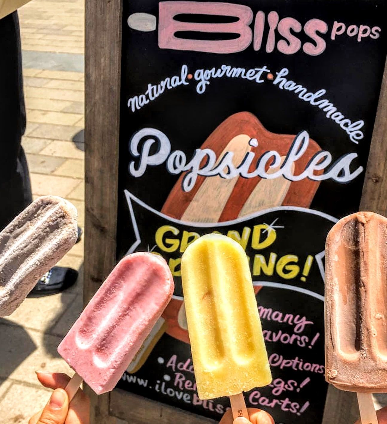 People holding popsicles in front of a bliss pops sign