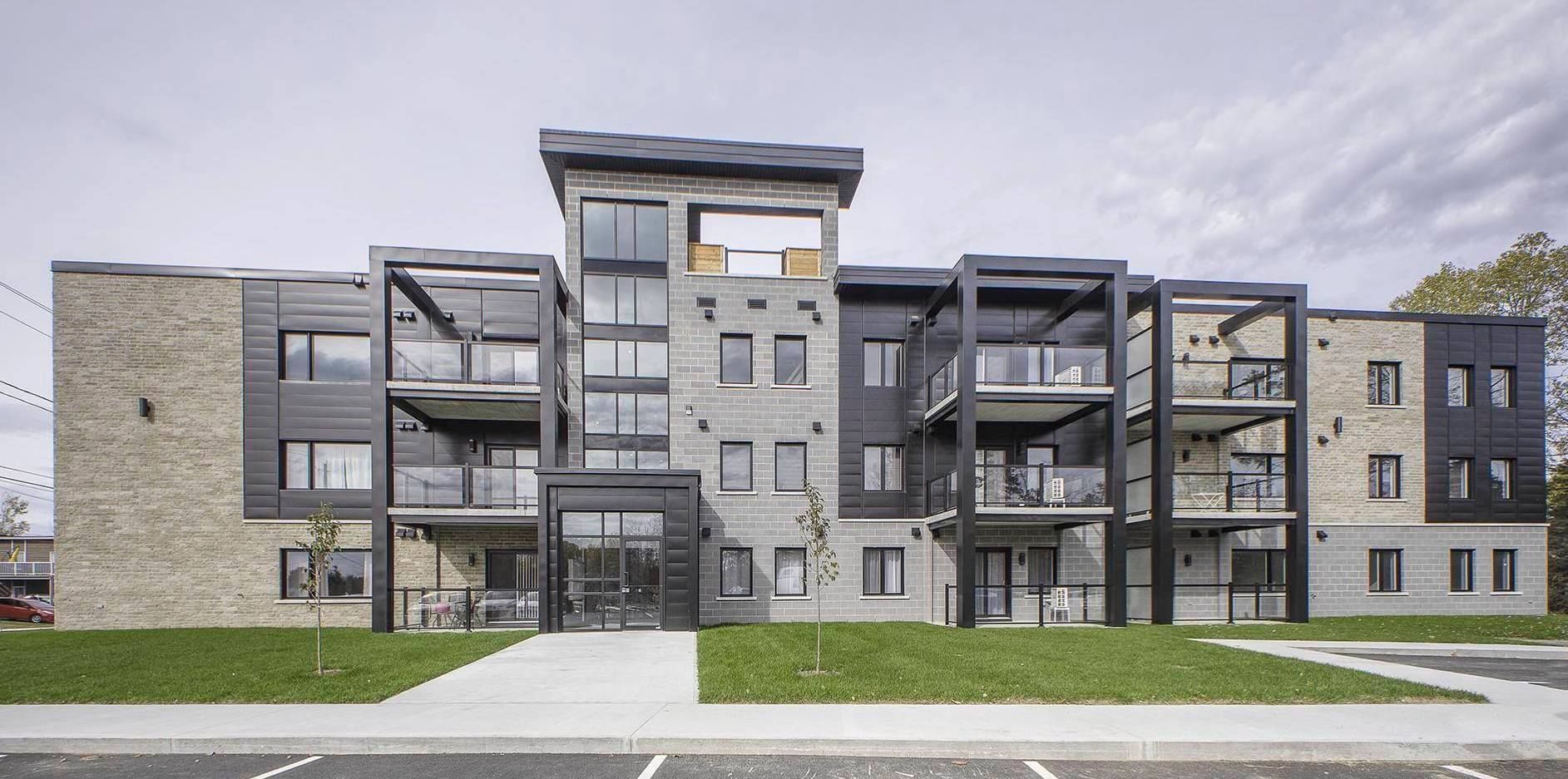 Immeuble moderne en pierre et bardage sombre, avec balcons. Gazon vert à l'avant.