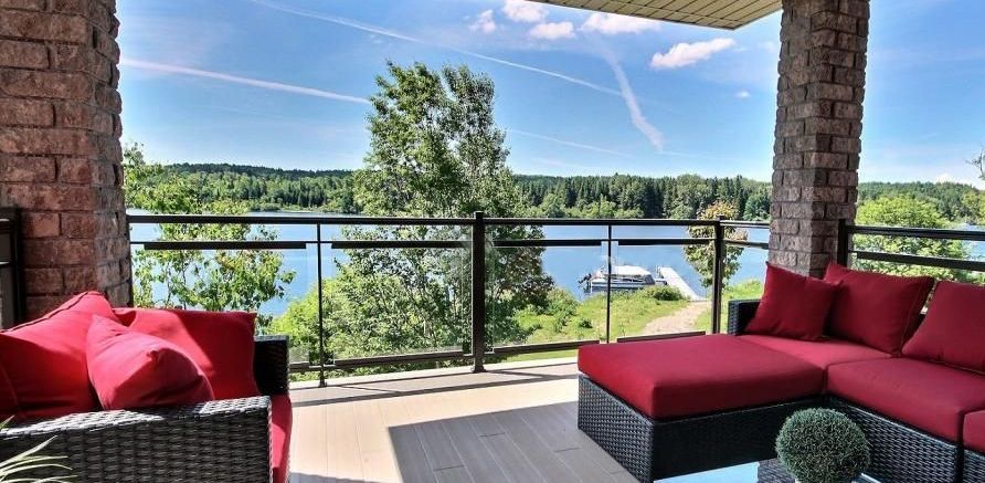Un porche avec des canapés rouges donnant sur un lac et des arbres par une journée ensoleillée.