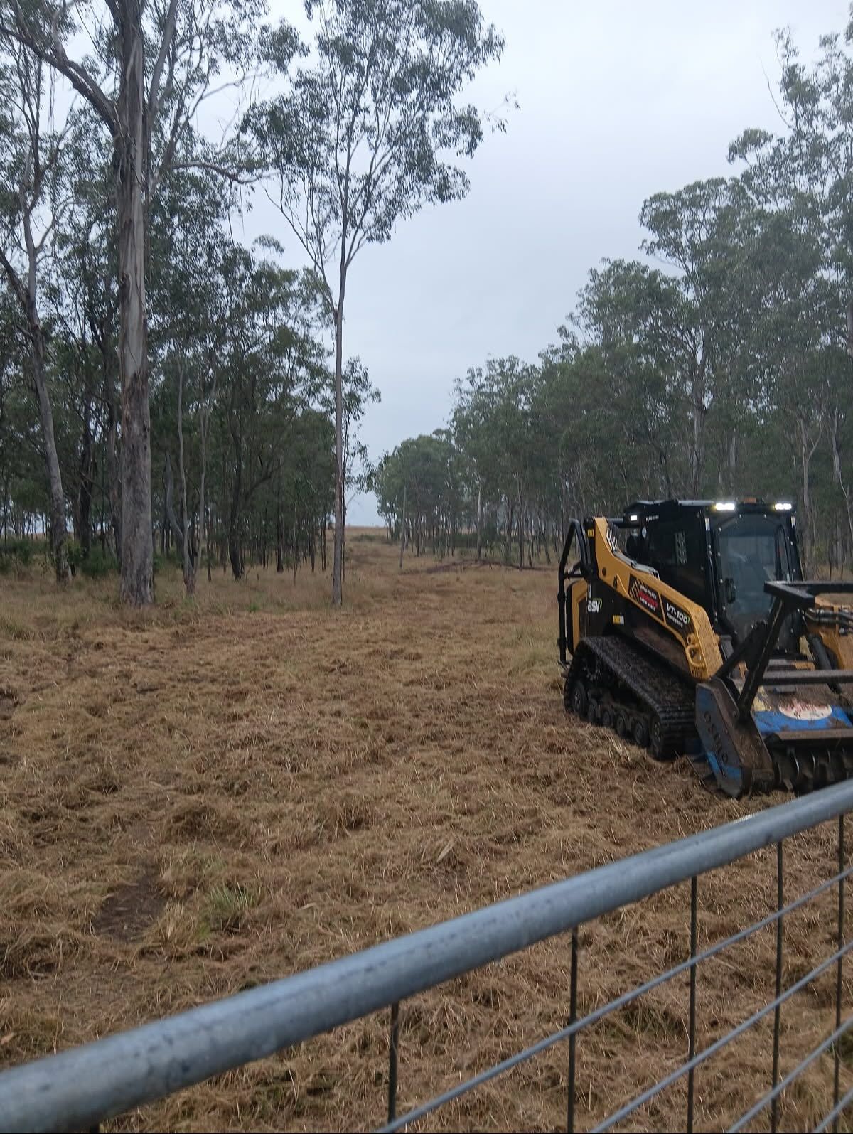Skid Steer Mulcher Clearing Brush in a Field Under a Cloudy Sky, Near Trees and a Fence — Dudgeon’s Earthworks in Murgon, QLD