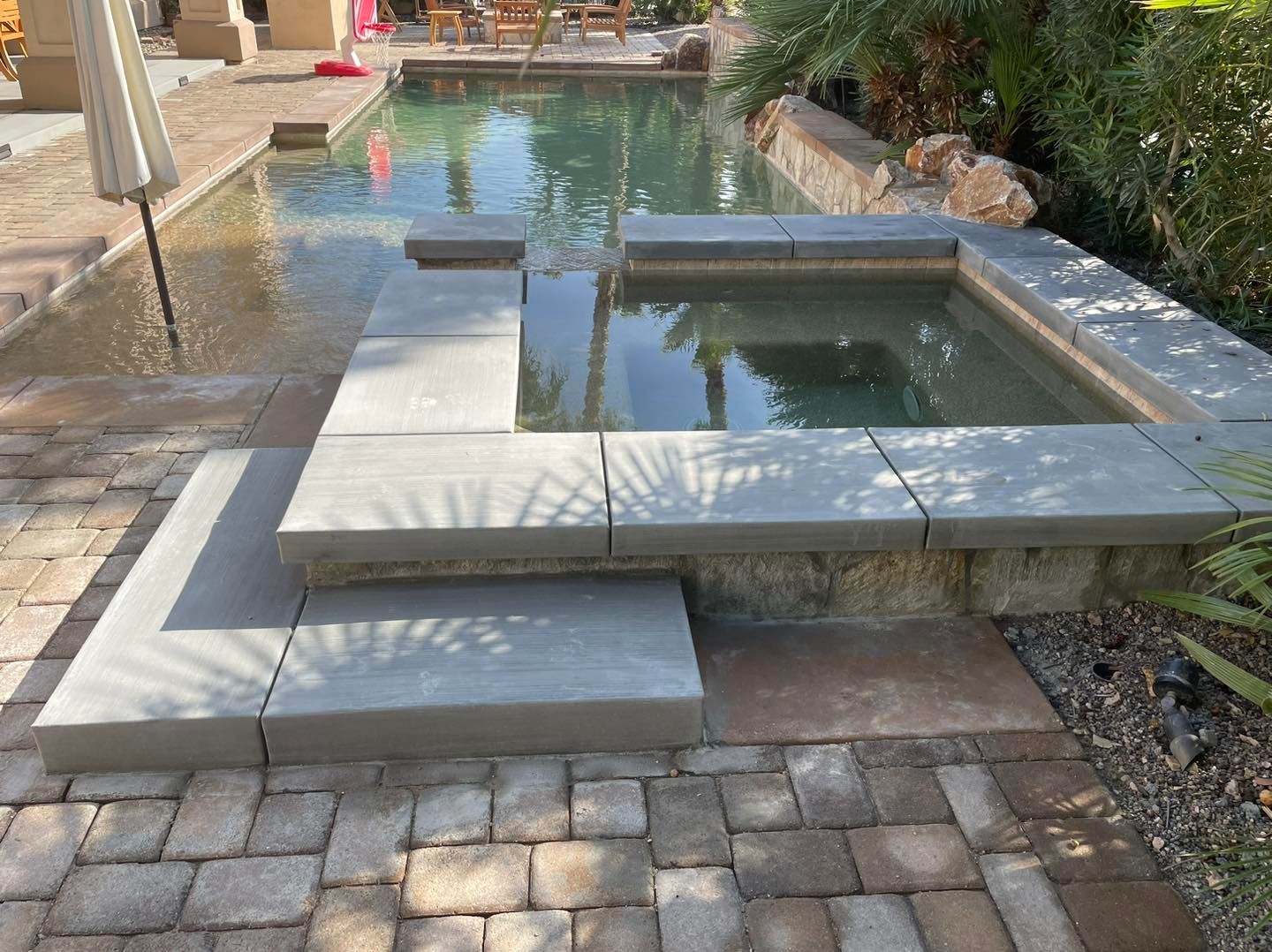 Image of an inviting backyard patio that includes a swimming pool, concrete slab next to the pool, and a concrete walkway. 