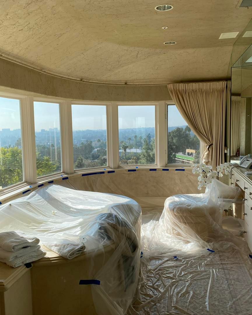 Image of a living room area with a beautiful view over the Coachella Valley, that is in process of an interior painting job. The furniture is covered in plastic wrap to deliver the best results fast and without damaging  anything. 