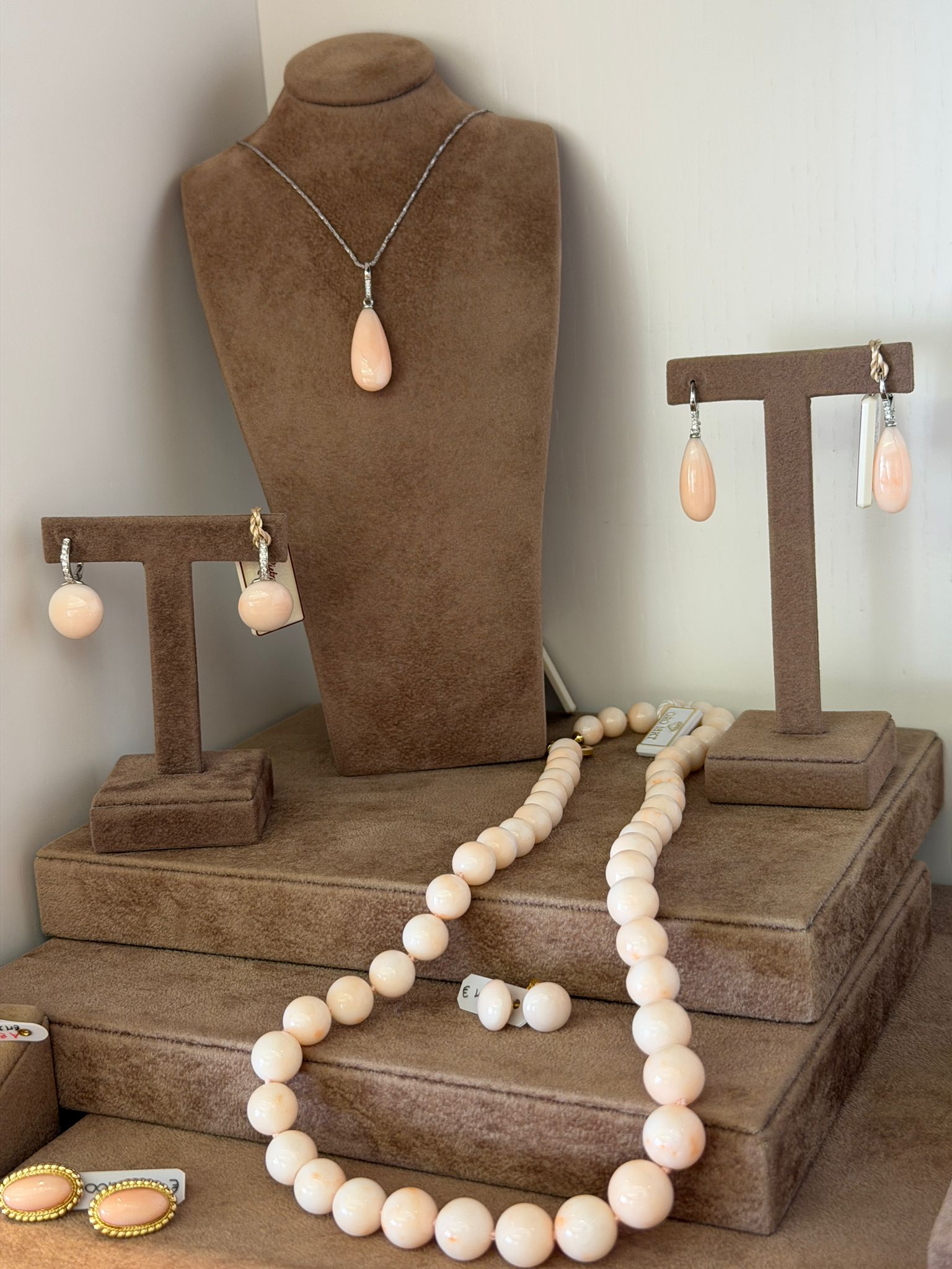 Espositore per gioielli beige con supporti per collane, collane di perle, orecchini e bracciali su una piattaforma marrone testurizzata.
