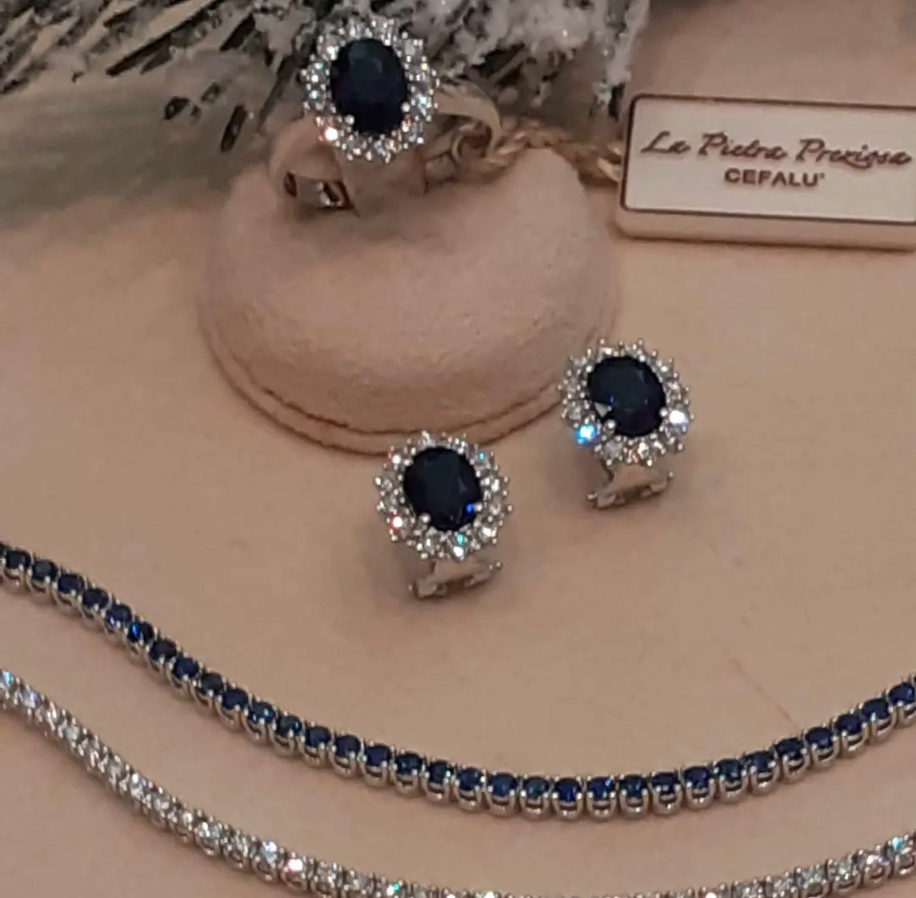 Set di gioielli con pietre preziose blu, composto da anello, orecchini e collana, esposto su un supporto.